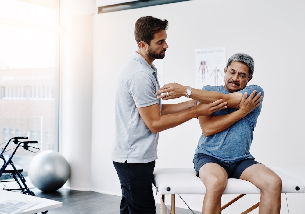 Physiotherapist, stretching and mature man in clinic, helping and healthcare with exercise and fitness. Hospital, workout and physiotherapy of patient, rehabilitation and concentration of person Physical Therapy